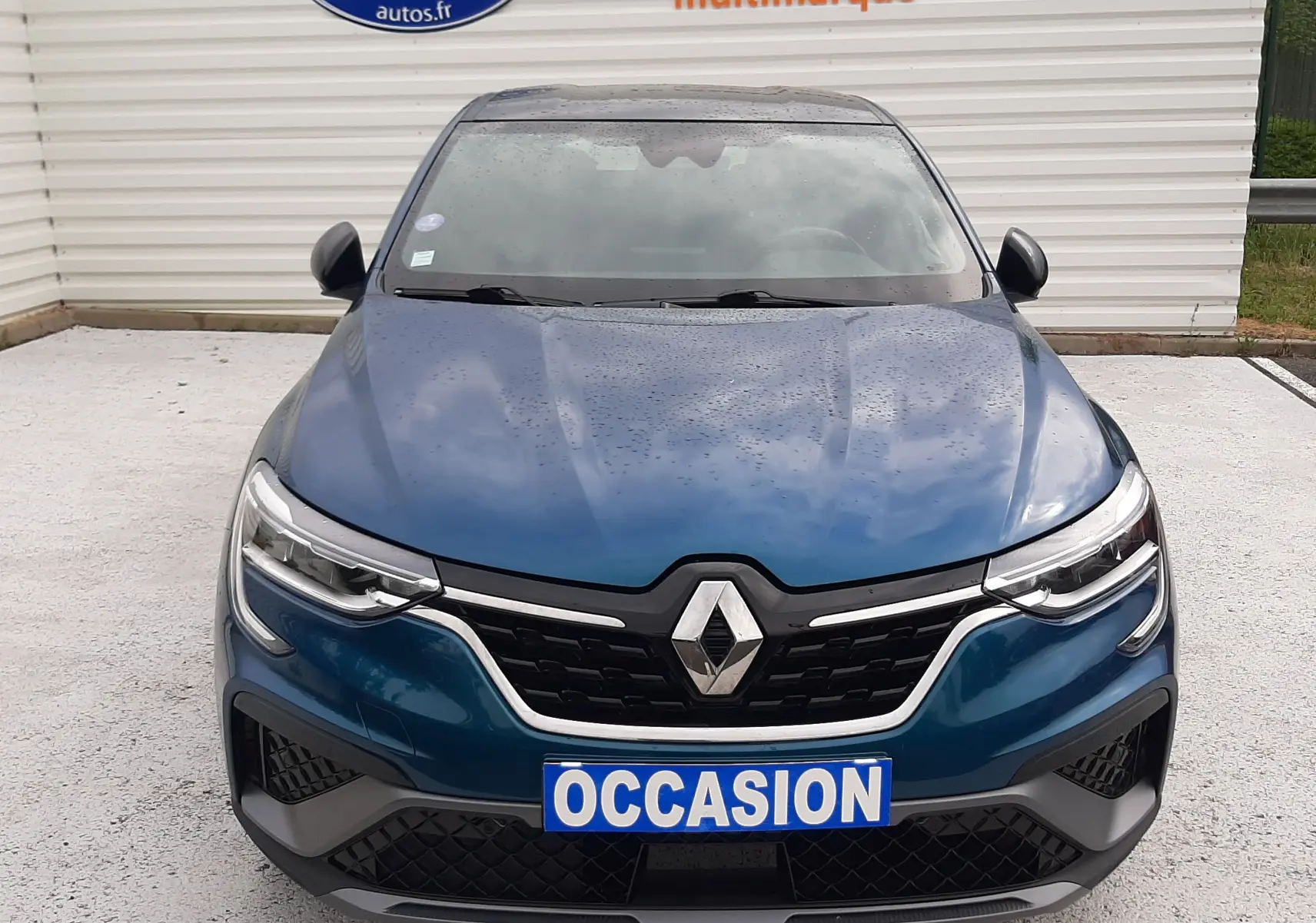 Vue avant d'une Renault Arkana E-Tech 145ch RS-Line bleu Zanzibar avec calandre noire et plaque "OCCASION".