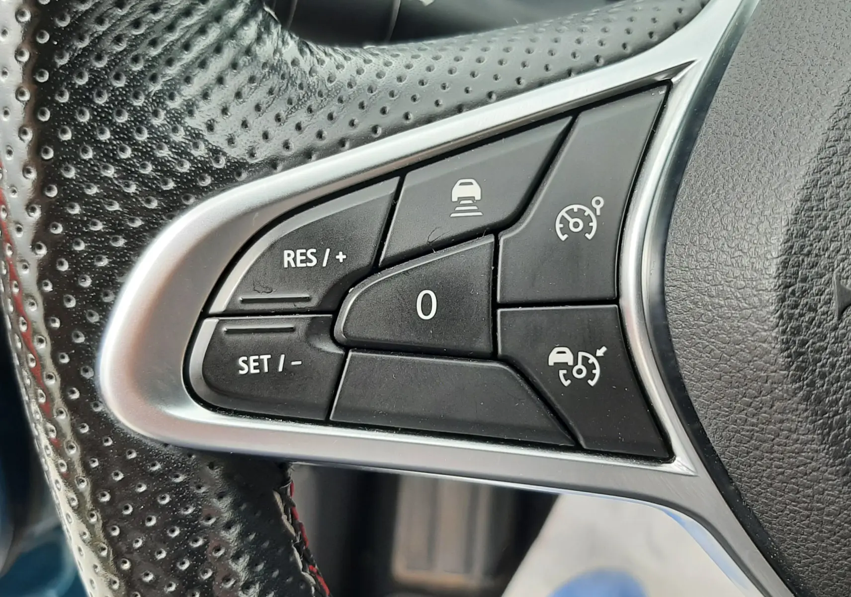 Gros plan sur les commandes noires du régulateur de vitesse au volant perforé de la Renault Arkana E-Tech.