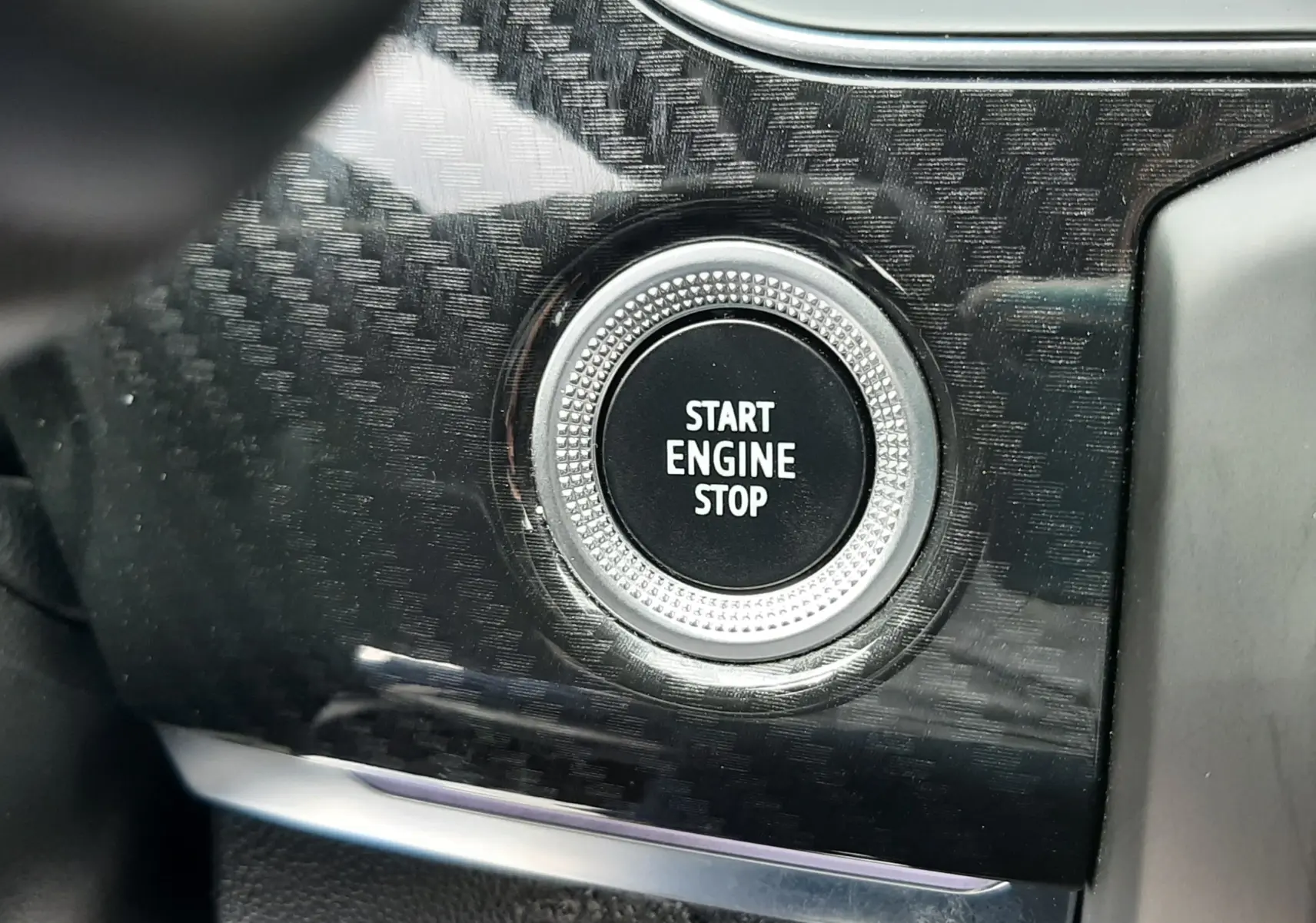 Gros plan sur le bouton start/stop moteur entouré d’un décor noir effet carbone dans le Renault Arkana E-Tech.