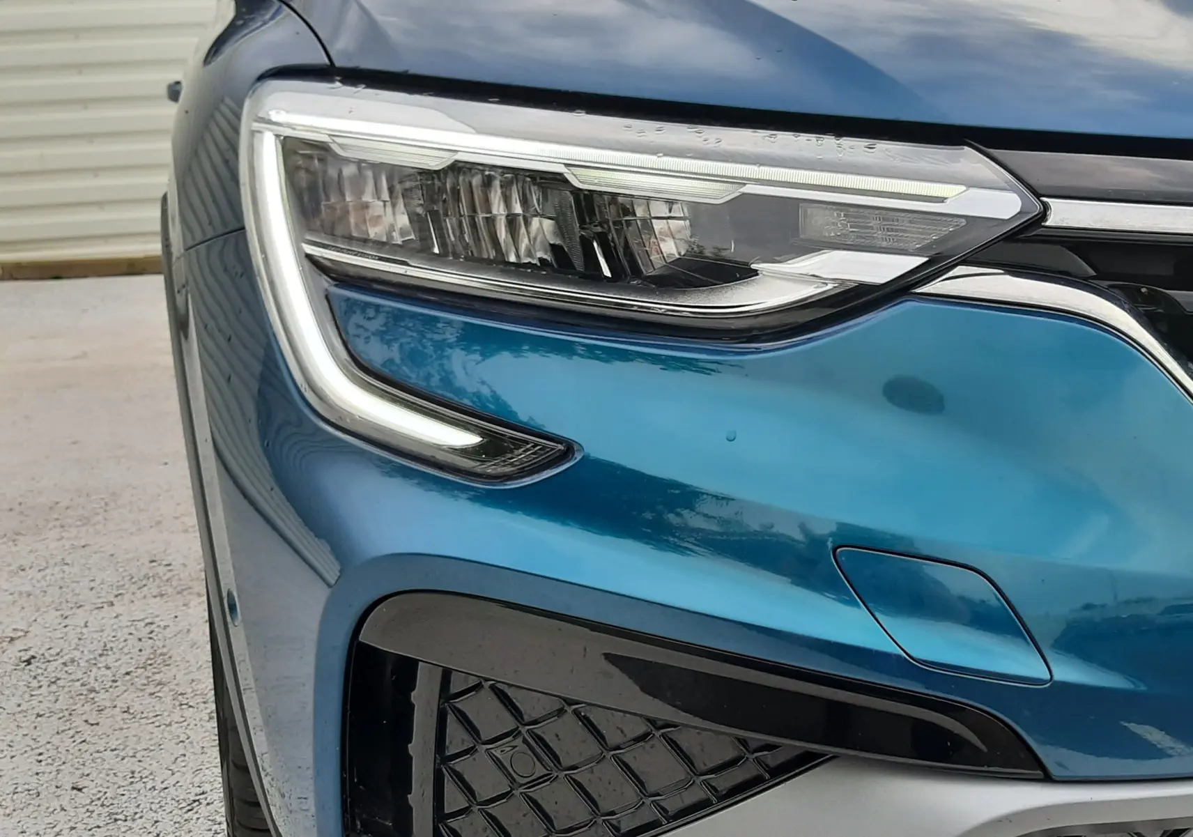 Gros plan sur l’avant gauche bleu Zanzibar du Renault Arkana E-Tech 145ch RS-Line, mettant en valeur le phare LED et la calandre.