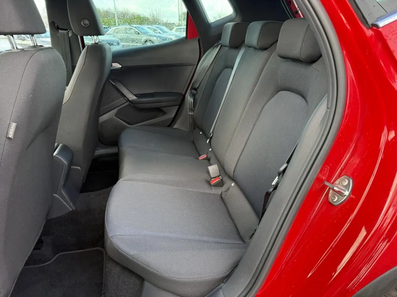 Vue intérieure côté arrière droit du SEAT Arona rouge 2024, montrant la banquette arrière en tissu gris foncé.