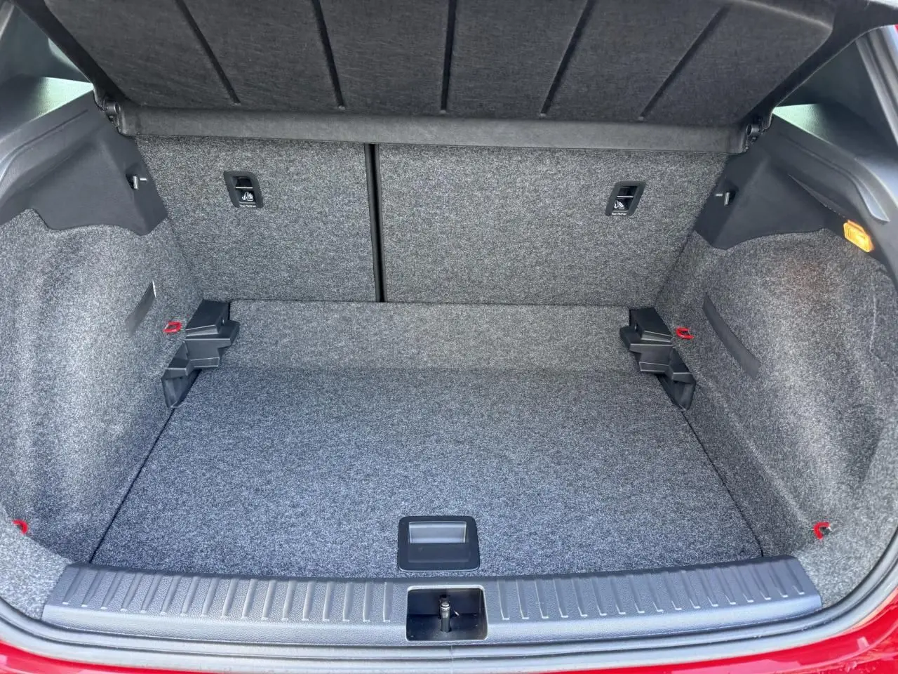Coffre ouvert vu de l'arrière d'une SEAT Arona rouge 2024, montrant un espace de chargement propre et tapissé gris.