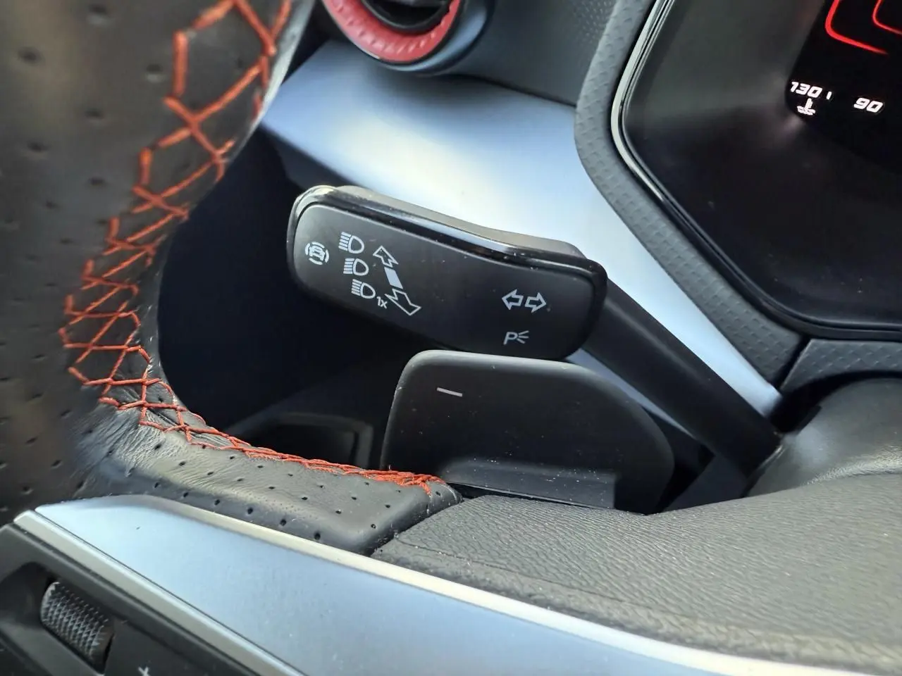 Gros plan sur le volant sport perforé noir avec surpiqûres rouges et la commande des clignotants du SEAT Arona 2024.
