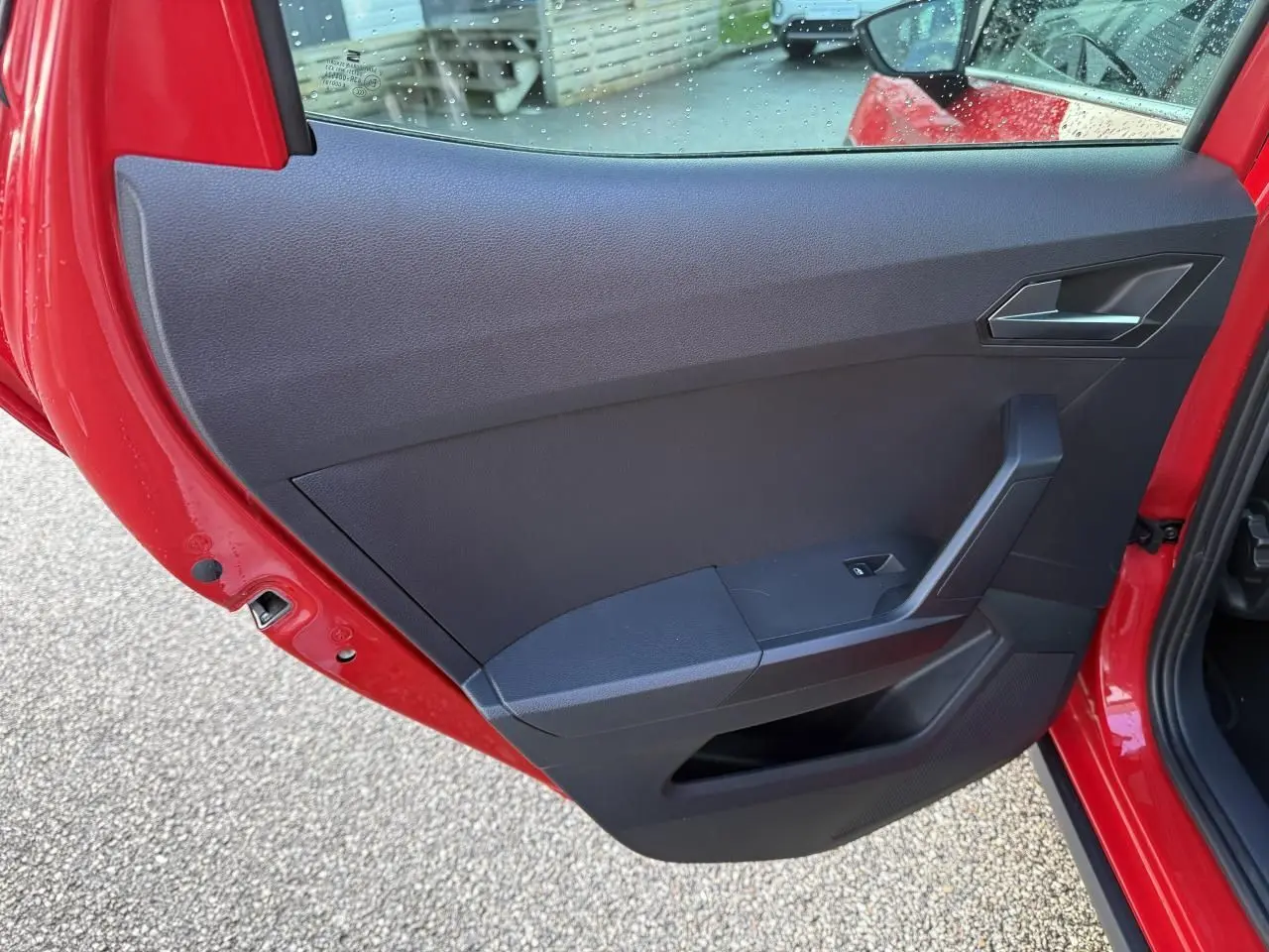 Vue rapprochée de la porte arrière gauche rouge du SEAT Arona 2024, montrant la garniture intérieure noire et la poignée.