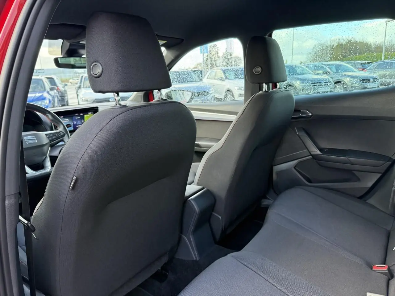 Vue intérieure arrière du SEAT Arona rouge 2024, montrant les sièges noirs et la console centrale entre les sièges avant.