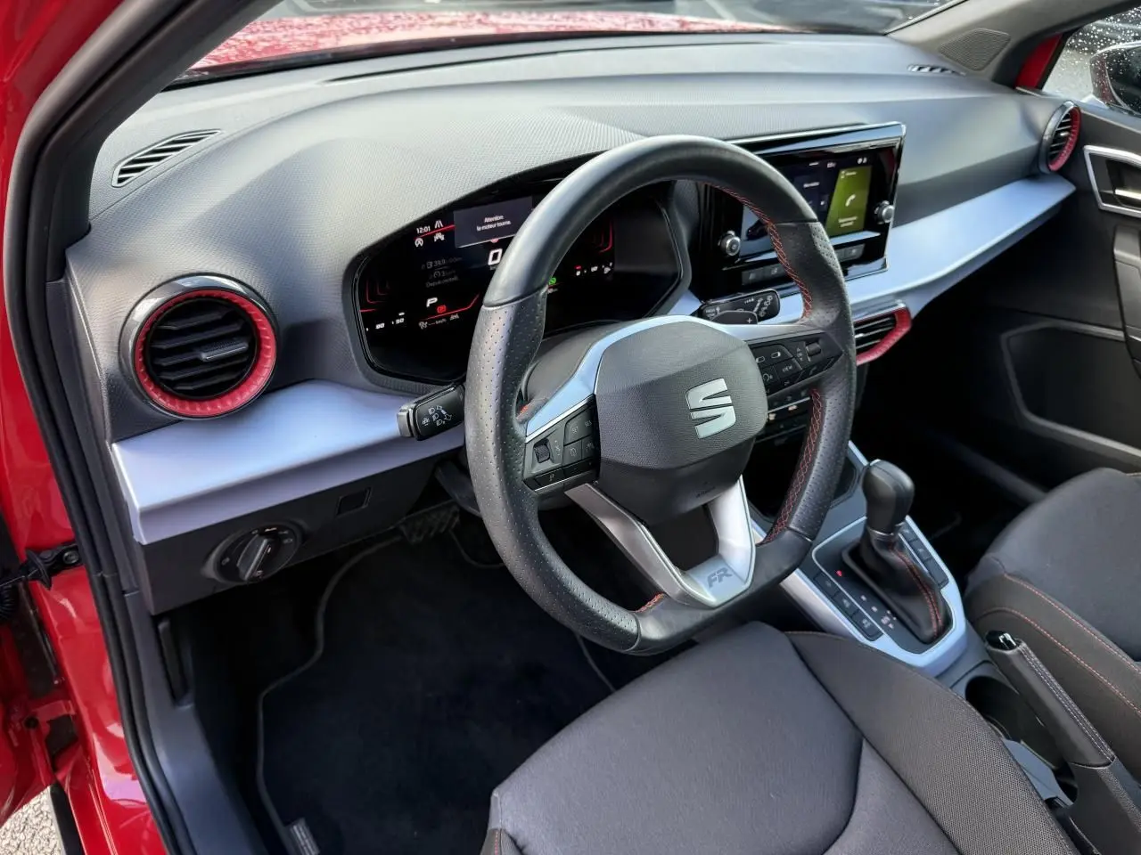 Vue intérieure côté conducteur du SEAT Arona rouge 2024, volant sport cuir Nappa avec surpiqûres rouges et tableau de bord digital.