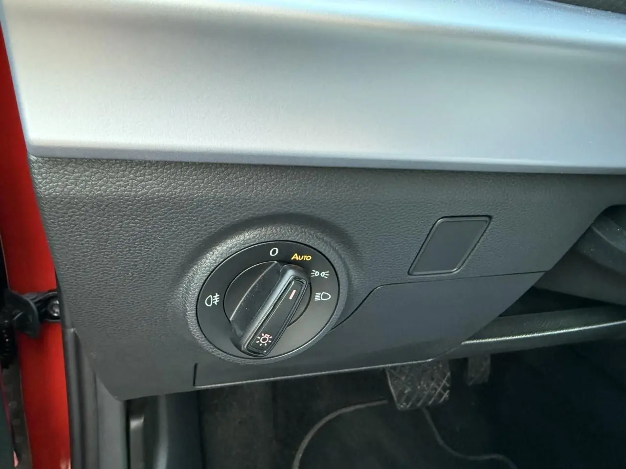 Détail du bouton de commande des phares sur le côté gauche du tableau de bord d’un SEAT Arona rouge 2024.
