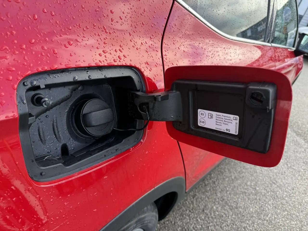 Vue rapprochée de la trappe à carburant rouge ouverte côté gauche d’un SEAT Arona 2024 avec gouttes d’eau.