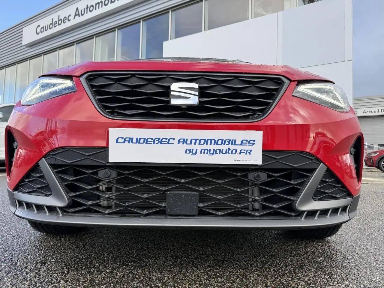 Vue avant rapprochée du SEAT Arona rouge 2024 avec calandre noire et phares Full LED allumés.