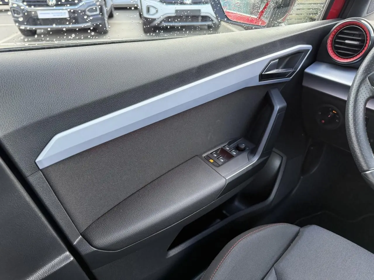 Vue intérieure côté gauche de la porte avant d'un SEAT Arona 2024 avec commandes électriques et habillage noir et gris.