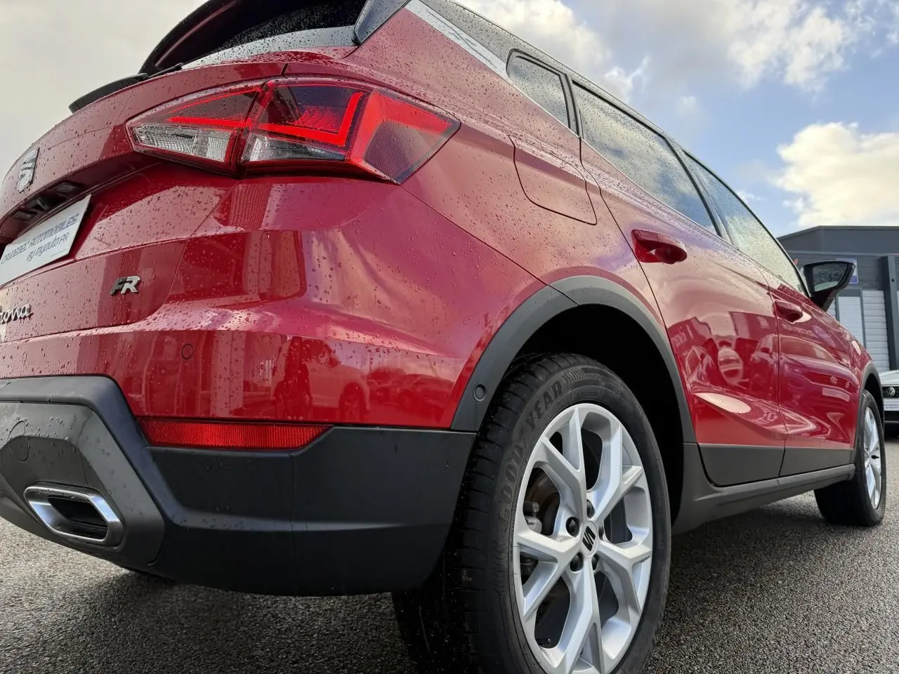 Vue 3/4 arrière droite d’un SEAT Arona rouge 2024 avec jantes alliage et feux arrière LED mouillés par la pluie.