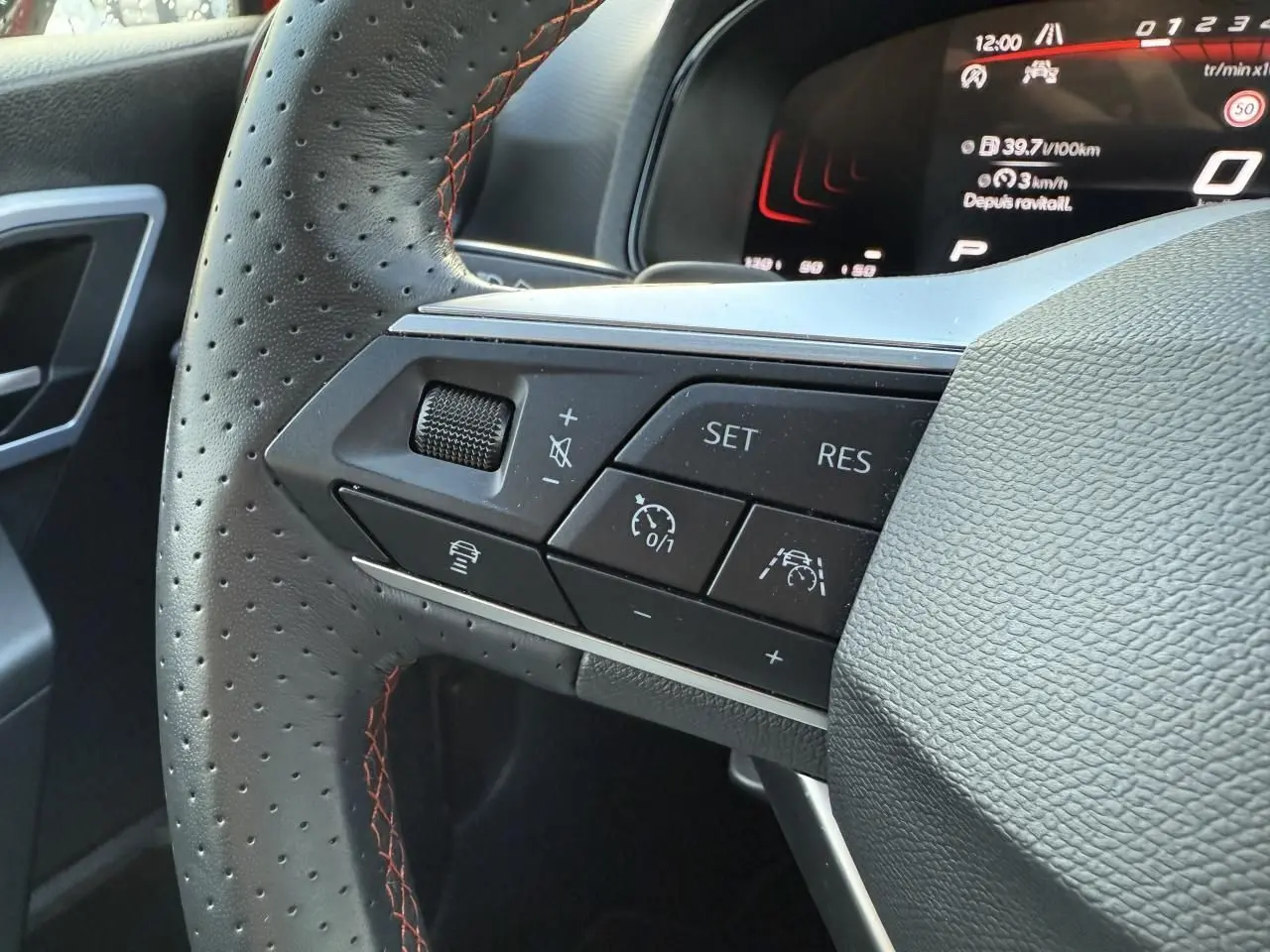 Gros plan sur le volant sport en cuir perforé avec surpiqûres rouges et commandes multifonctions du SEAT Arona 2024.