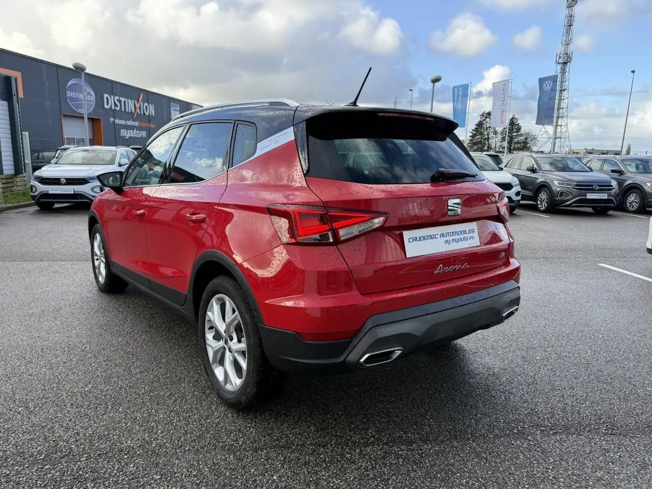 Vue 3/4 arrière droite d'un SEAT Arona rouge avec vitres surteintées et feux arrière LED, stationné sur parking humide.