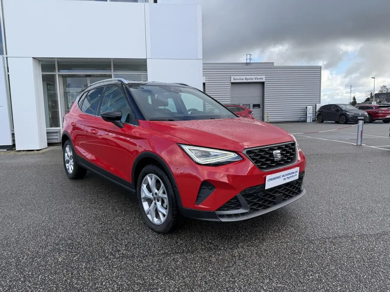 SEAT Arona rouge vue 3/4 avant droit, avec projecteurs LED et calandre noire, stationné devant un bâtiment.