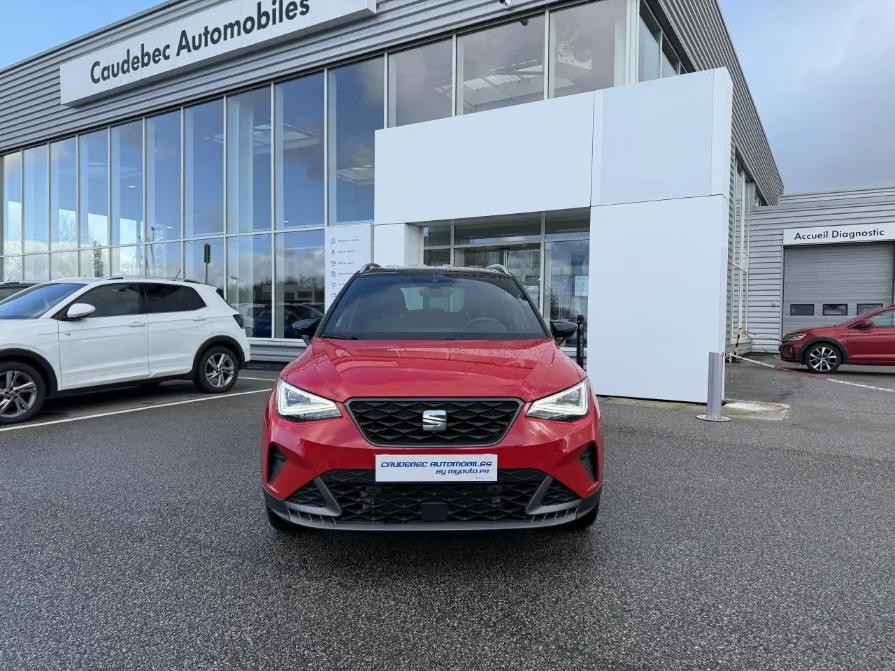 Vue frontale d’un SEAT Arona rouge avec calandre noire et projecteurs Full LED, stationné devant un concessionnaire.