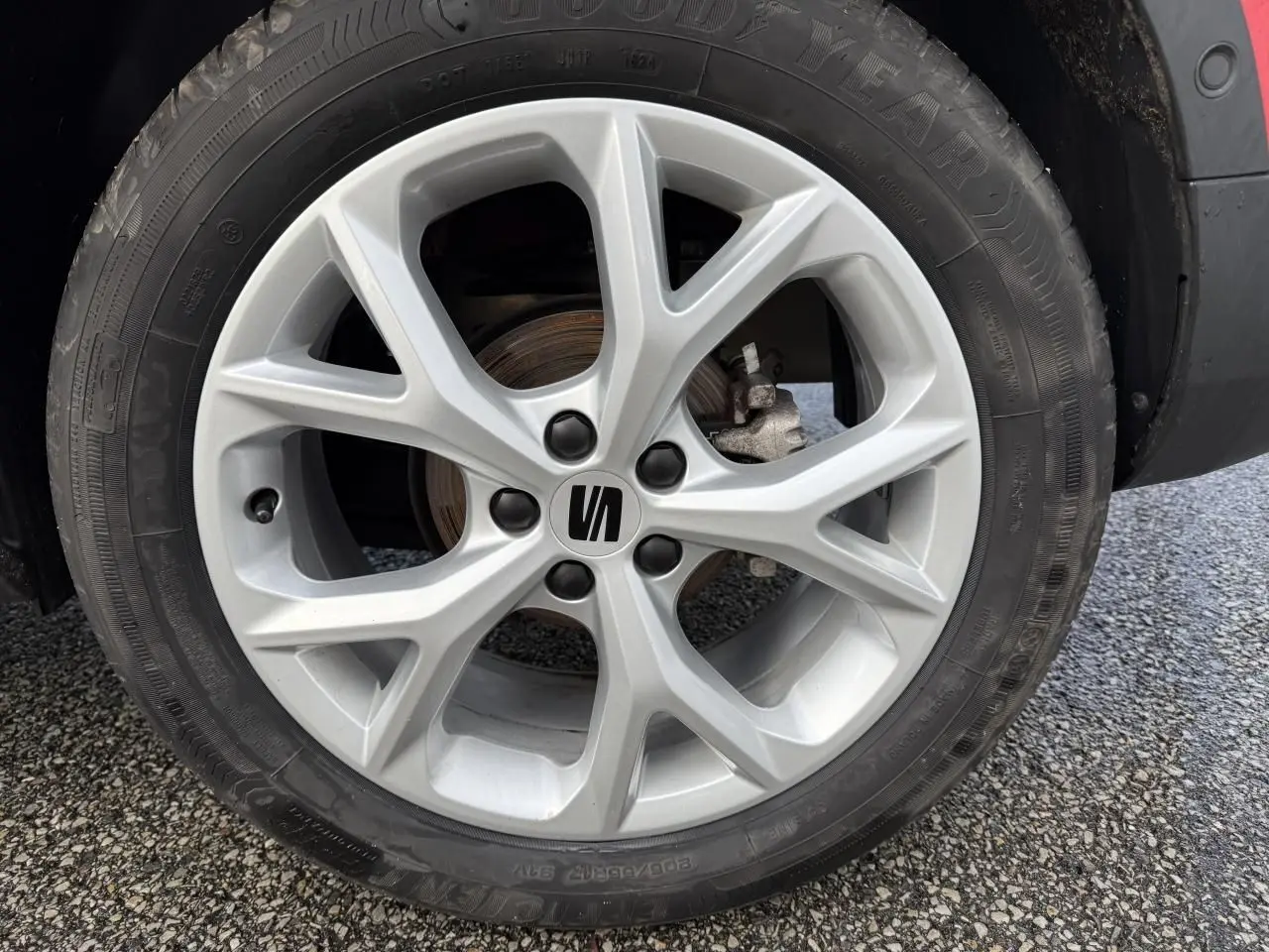 Gros plan sur la roue avant droite d'une SEAT Arona rouge, mettant en valeur la jante alliage argentée au design moderne.