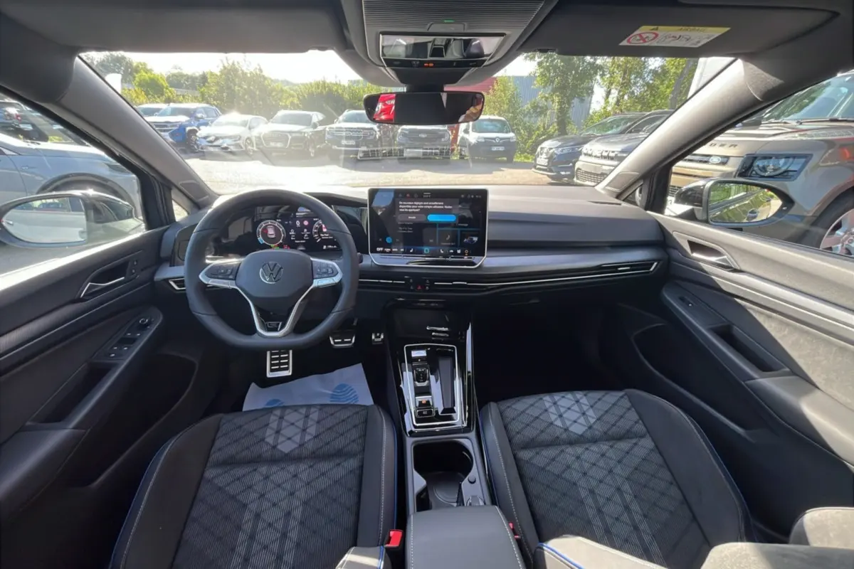 Vue intérieure avant de la Volkswagen Golf E-TSI 150 R-Line 2026, avec tableau de bord numérique et sièges tissu gris.