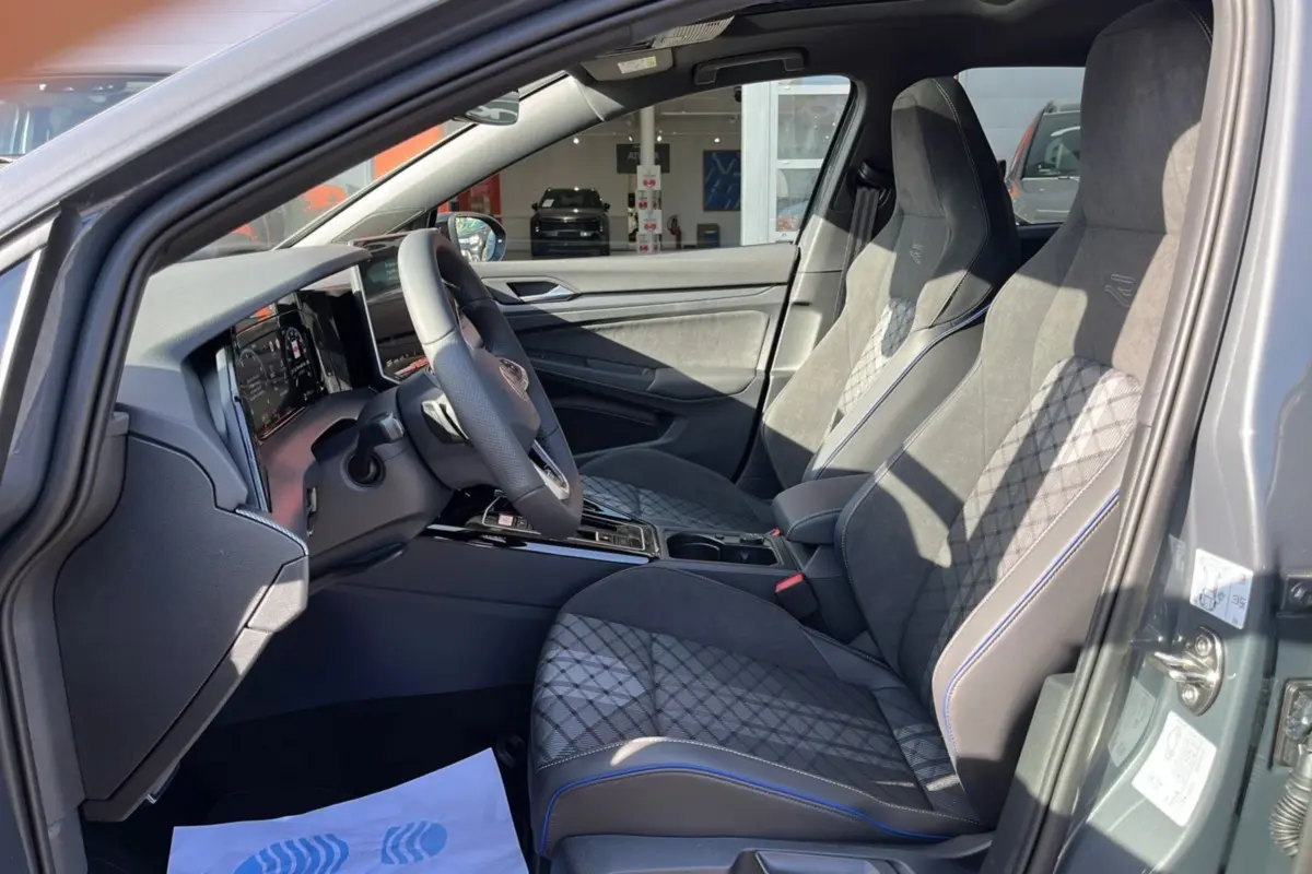 Vue intérieure côté conducteur de la Volkswagen Golf gris dauphin, sièges sport R-Line avec surpiqûres bleues et volant cuir multifonctions.