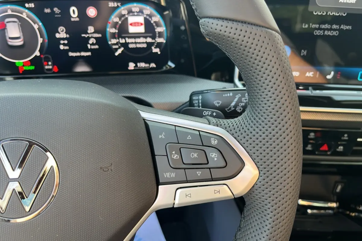 Gros plan sur le volant cuir perforé multifonctions de la Volkswagen Golf gris dauphin, avec tableau de bord numérique en arrière-plan.