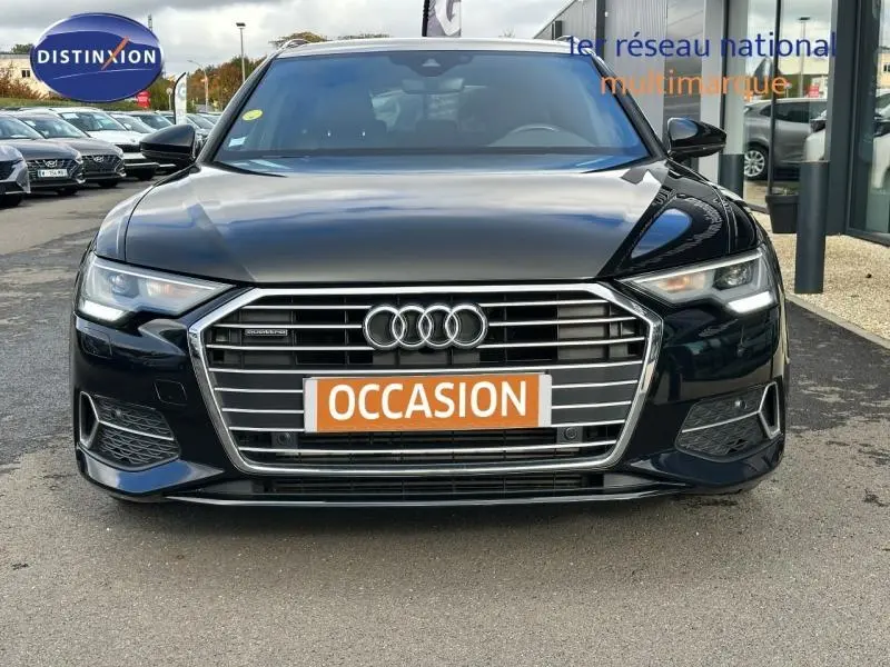 Vue frontale d'une Audi A6 Avant 45 TDI S line noire métal avec calandre chromée et phares LED allumés.