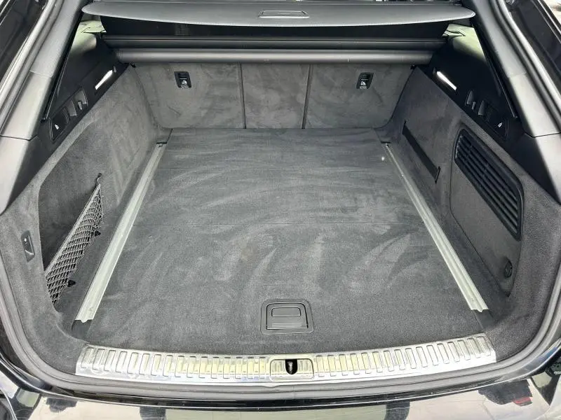 Coffre spacieux vu de l'arrière d'une Audi A6 Avant noir métal, avec tapis gris et finitions métalliques.