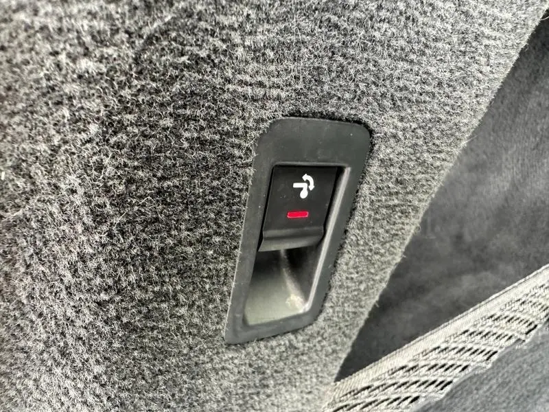 Gros plan sur le bouton d'ouverture électrique du coffre dans l'habitacle de l'Audi A6 Avant noir métal.