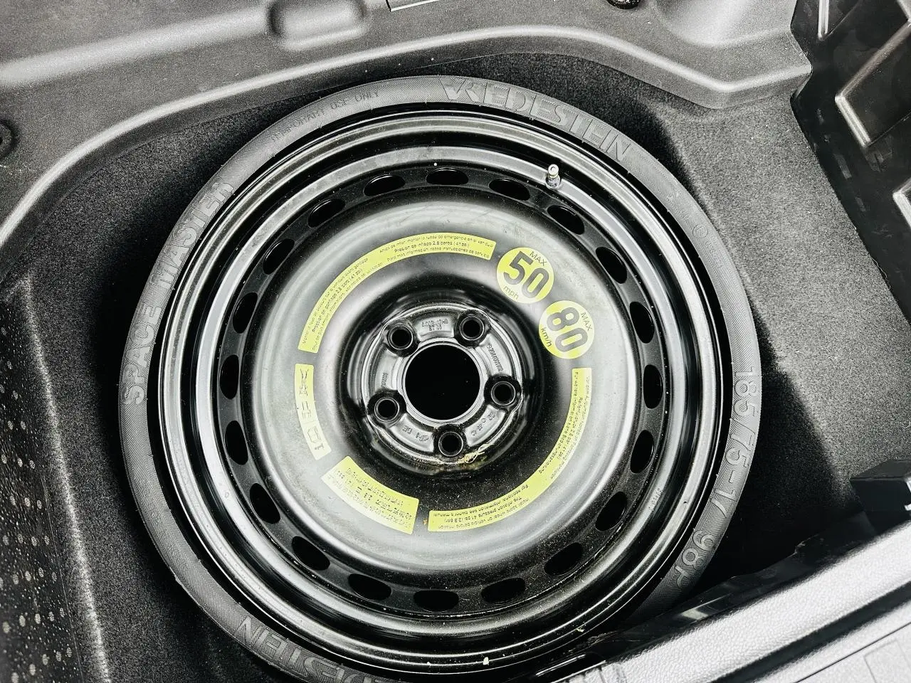 Gros plan sur la roue de secours compacte noire dans le coffre du Mercedes GLK 220 CDI 4-Matic noir de 2010.