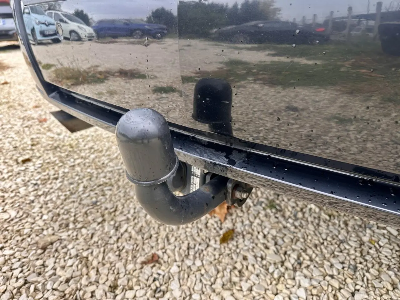 Gros plan sur l'attelage noir à l'arrière d'un Mercedes GLK 220 CDI noir, reflétant le sol gravillonné.