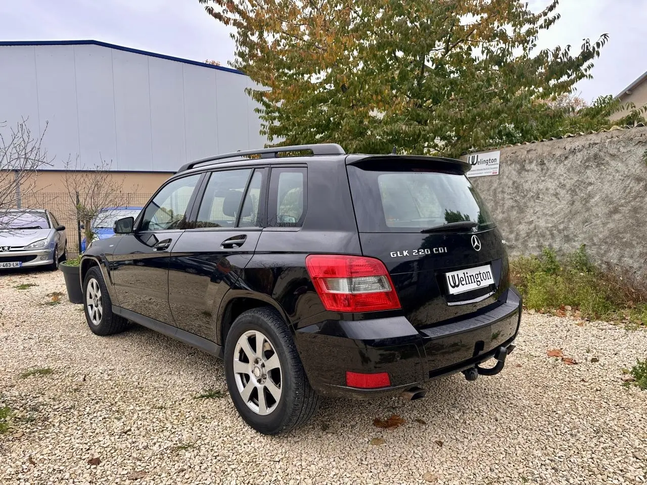 Vue 3/4 arrière droite d'un Mercedes GLK 220 CDI noir avec barres de toit et attelage visible.