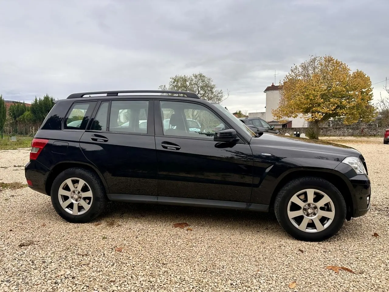 Profil côté gauche d'un Mercedes GLK noir 2010 garé sur un sol gravillonné avec toit ouvrant et jantes argentées.