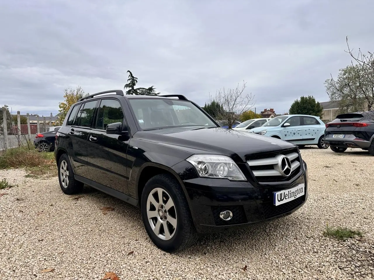 Mercedes GLK noir vue 3/4 avant droit sur parking avec calandre et jantes argentées visibles.