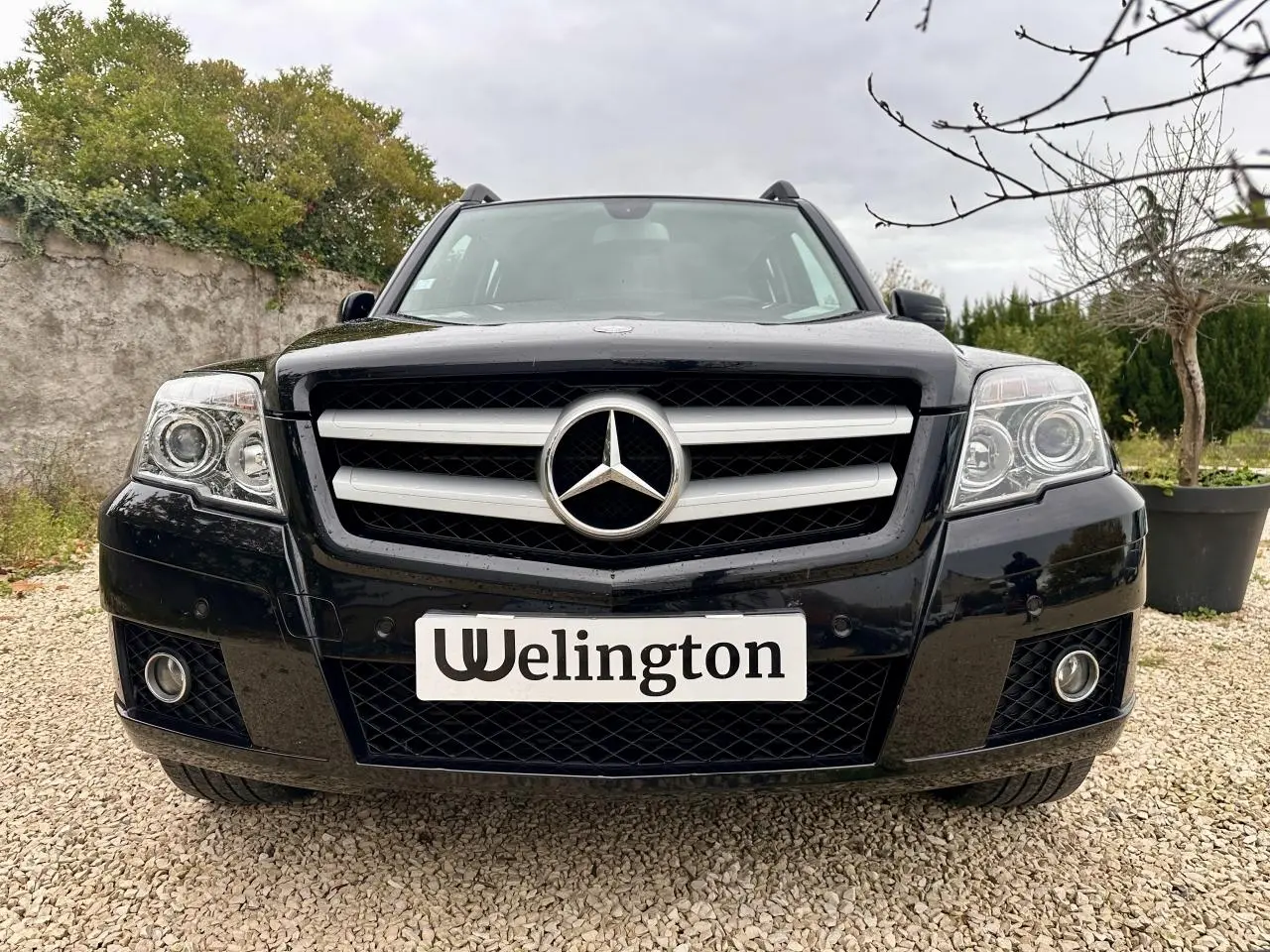Vue avant d'un Mercedes GLK noir 2010 avec calandre chromée et logo étoile bien visible sur fond extérieur.