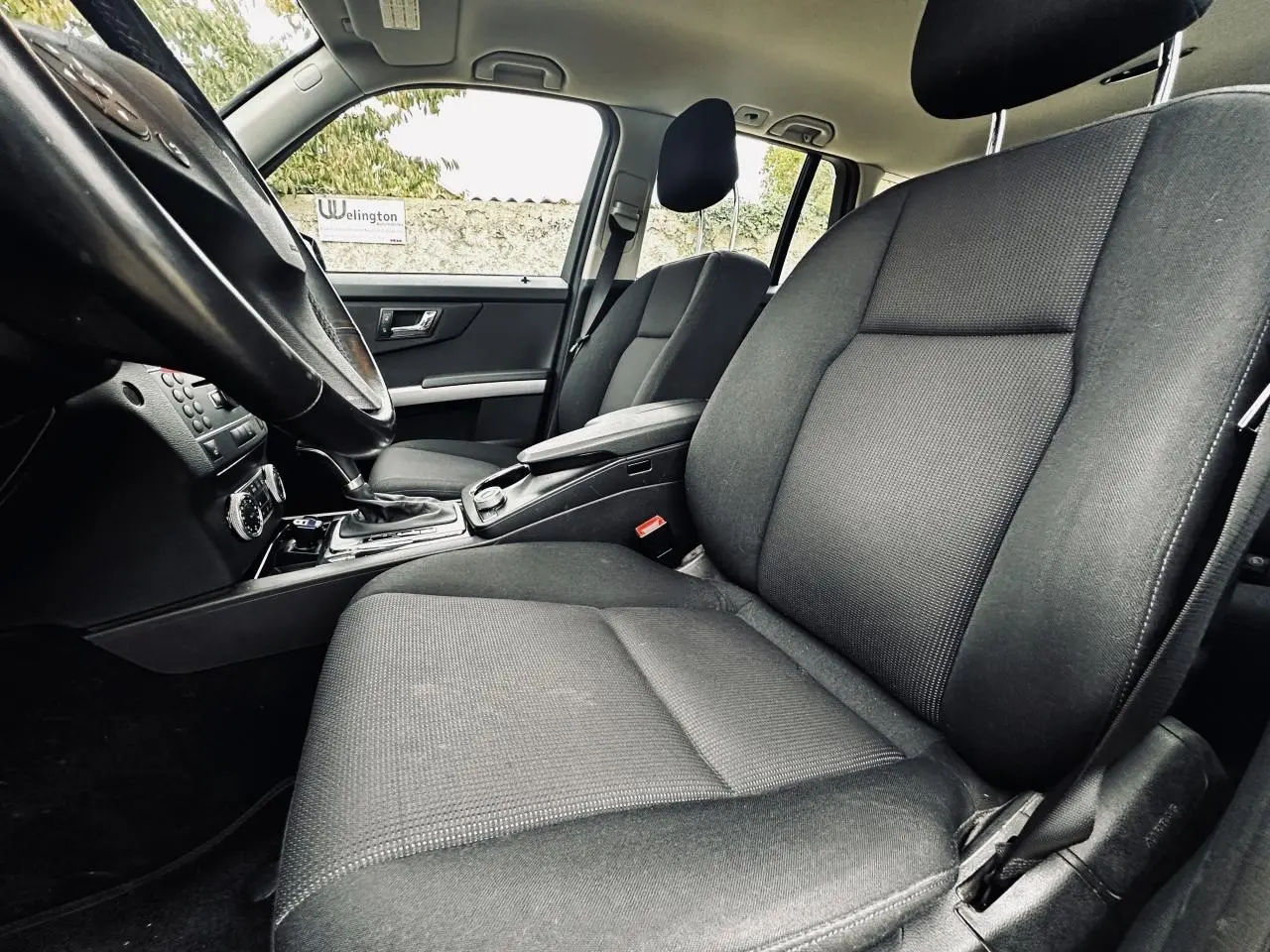 Vue intérieure côté conducteur du Mercedes GLK 220 CDI noir de 2010, mettant en valeur les sièges avant en tissu gris foncé.