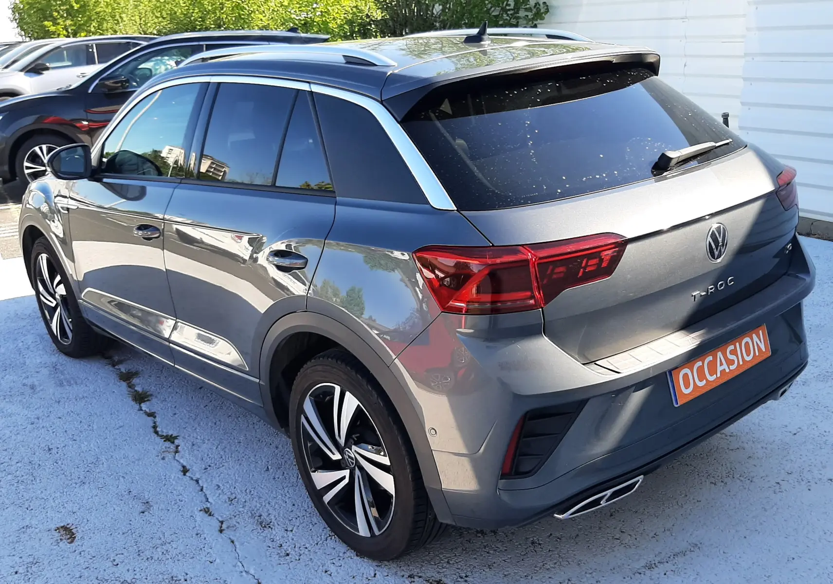 Volkswagen T-Roc gris Indium en 3/4 arrière droit, avec jantes alliage et badge R-Line visible.