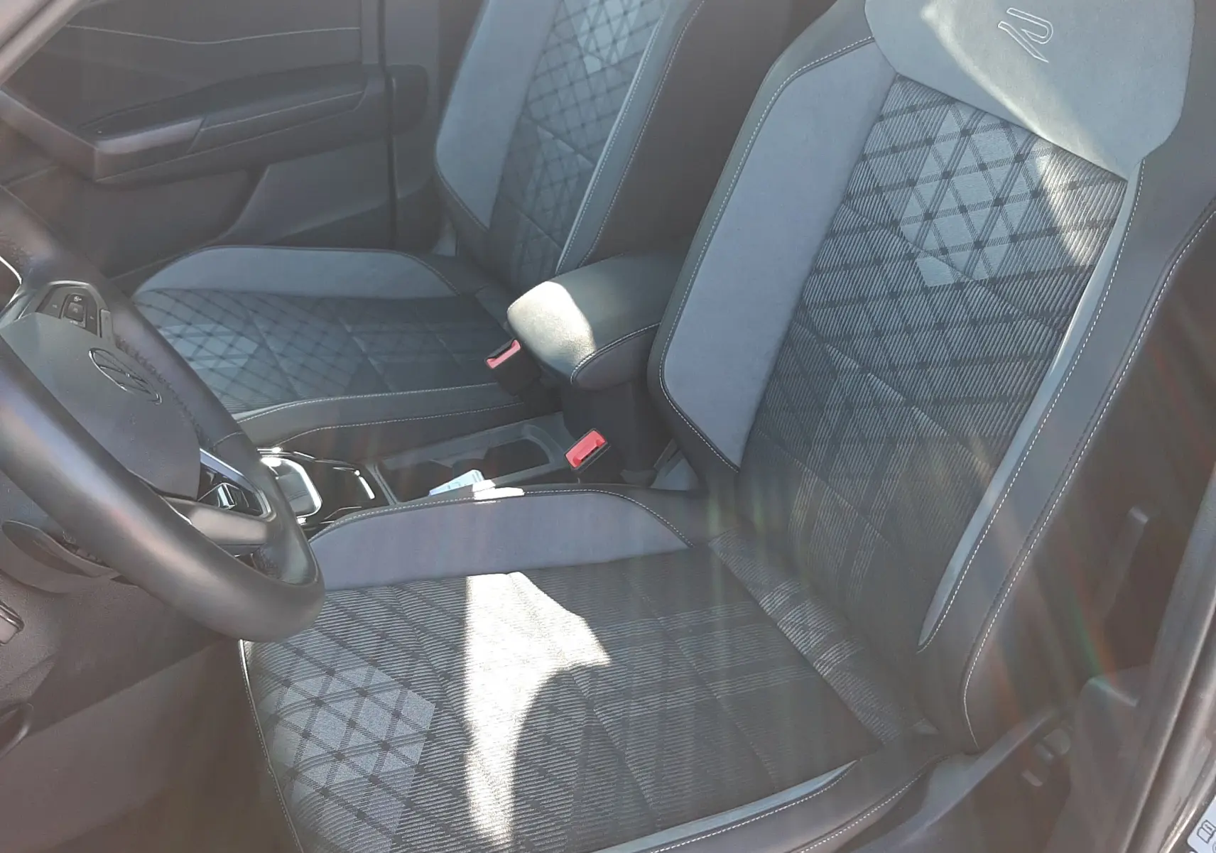 Vue intérieure côté conducteur du Volkswagen T-Roc 2024, sièges gris avec surpiqûres et logo R brodé sur les appuie-têtes.
