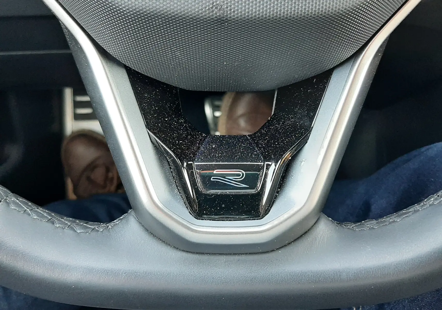 Gros plan sur le volant du Volkswagen T-Roc 2024 gris Indium, mettant en valeur le logo R et l'airbag central.