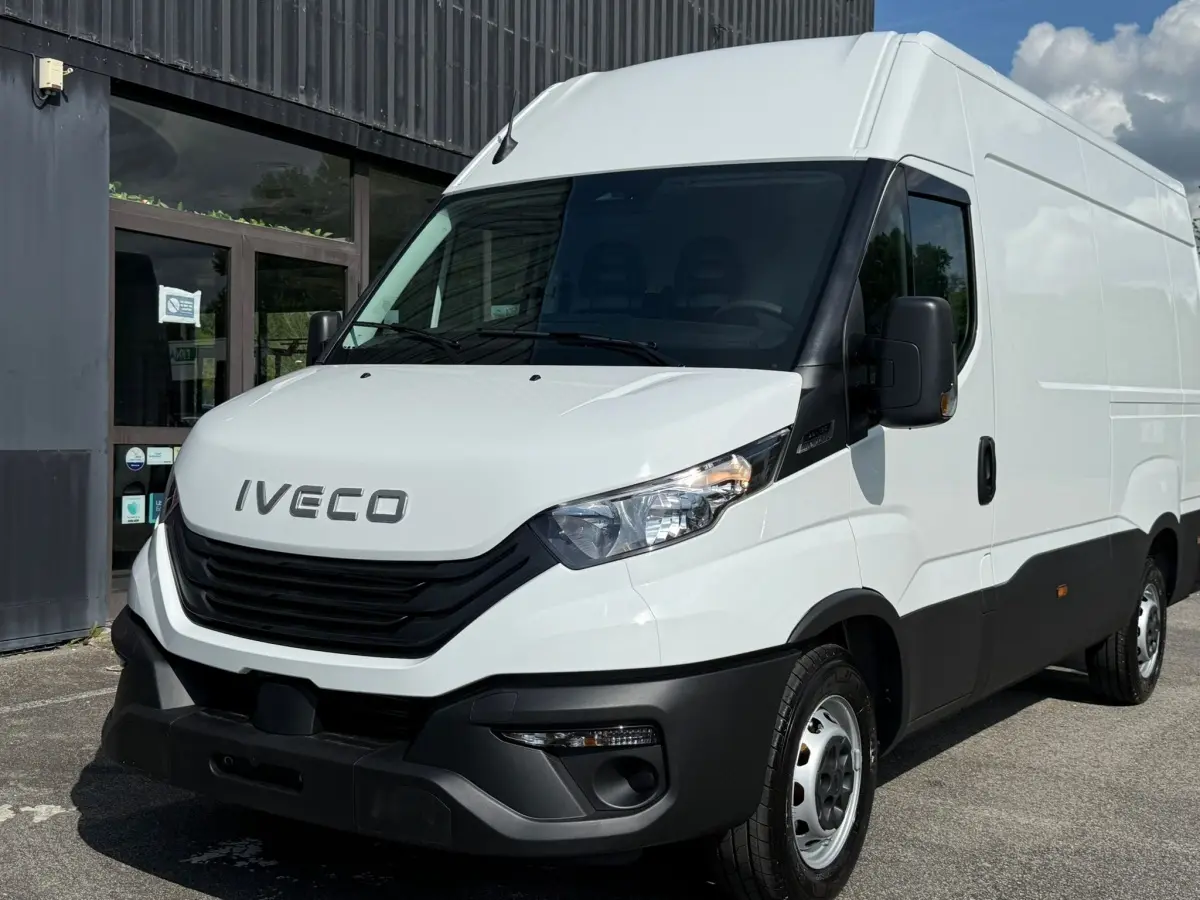 Vue 3/4 avant d’un utilitaire Iveco Daily blanc avec calandre noire et pare-chocs avant robuste, stationné devant un bâtiment.
