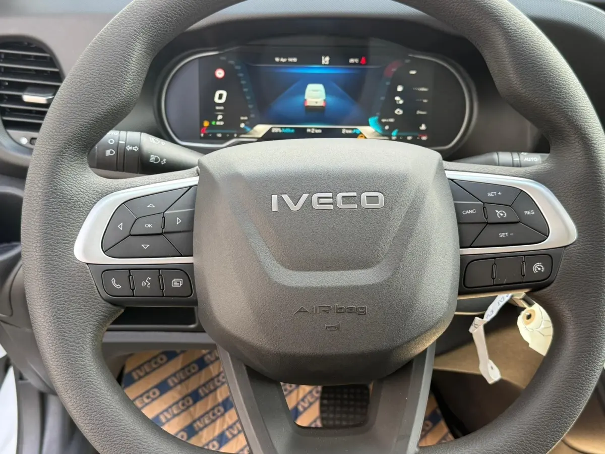 Vue rapprochée du volant noir de l’Iveco Daily 2026 avec commandes intégrées et tableau de bord numérique en arrière-plan.