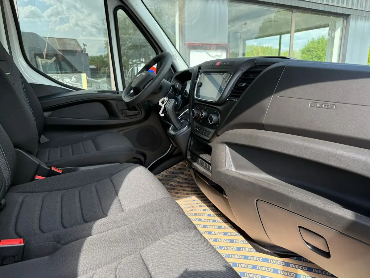 Vue intérieure côté conducteur de l’Iveco Daily blanc 2026, montrant le tableau de bord et les sièges en tissu gris.