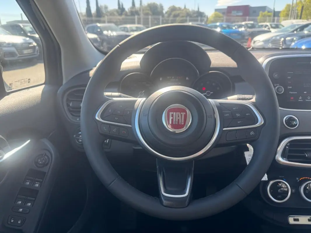 Vue intérieure centrée sur le volant noir avec logo FIAT, tableau de bord et commandes de la Fiat 500X bleu 2024.