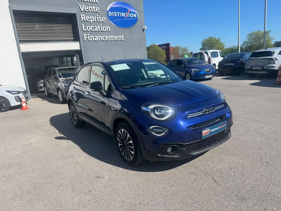 Fiat 500X bleu vue 3/4 avant droit, avec jantes 16 pouces classiques et phares ronds allumés.