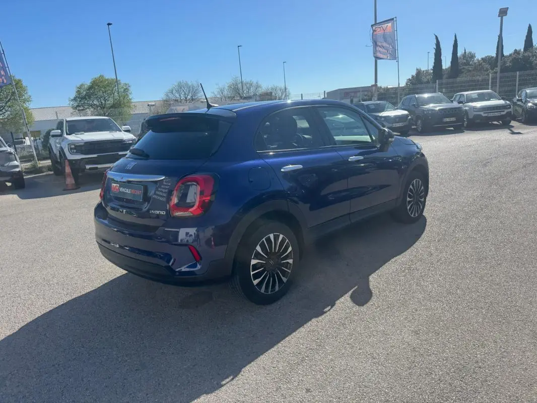 Vue 3/4 arrière droite d'une FIAT 500X bleu foncé avec jantes classiques 16 pouces, stationnée en extérieur.