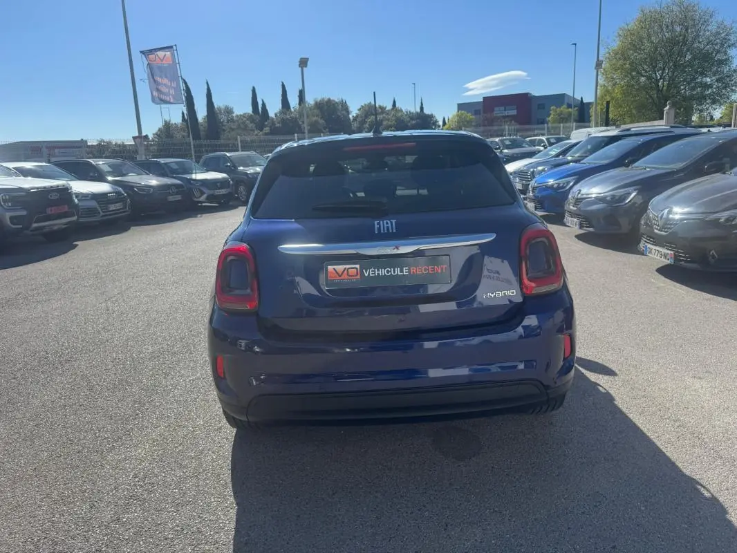 Vue arrière d'une Fiat 500X bleu foncé hybride 2024, avec feux arrière rouges et vitres teintées.