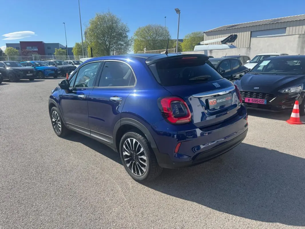 Vue 3/4 arrière droite d'une FIAT 500X bleu métallisé avec jantes classiques 16 pouces sur parking extérieur.