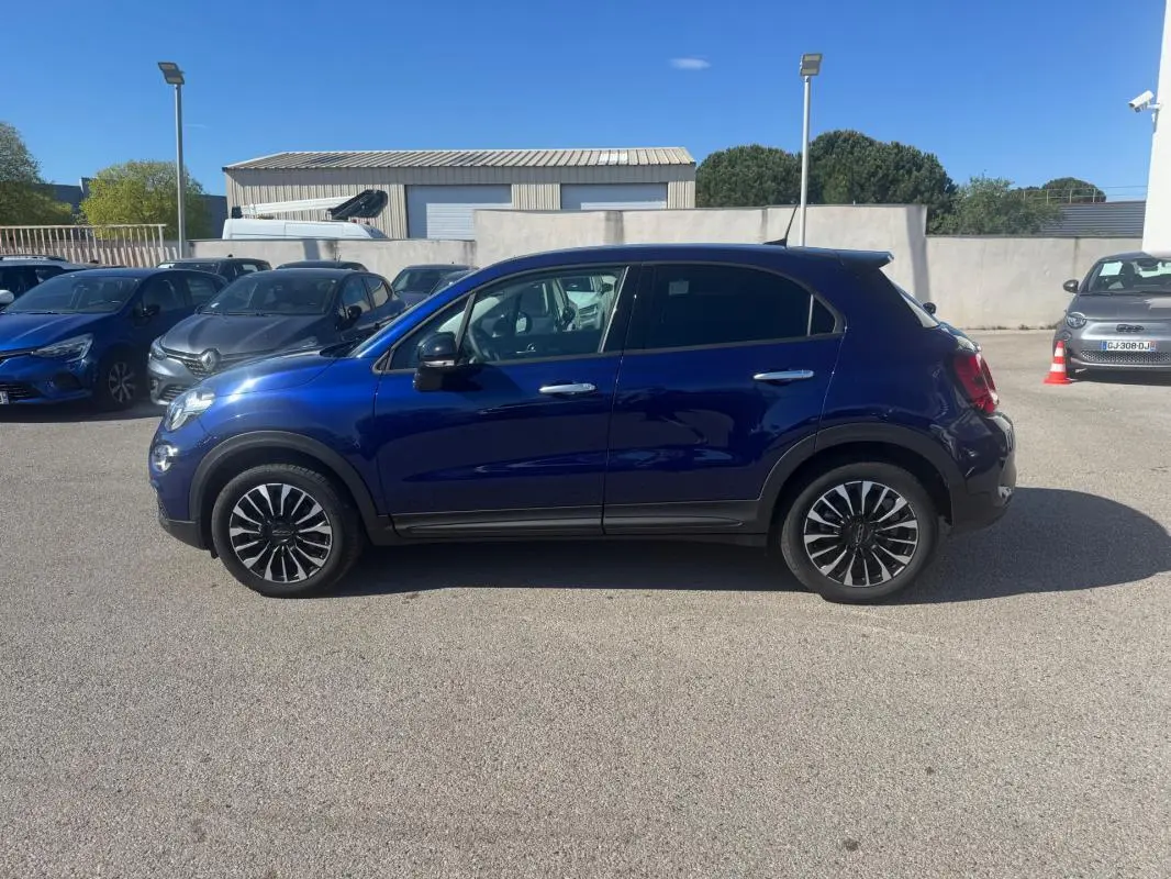 Profil droit d'un FIAT 500X bleu MY23 avec jantes classiques 16 pouces sur parking extérieur ensoleillé.