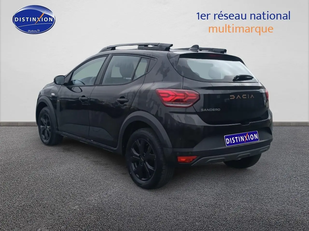Vue 3/4 arrière droite d'une Dacia Sandero noire avec barres de toit et jantes noires sur fond neutre.