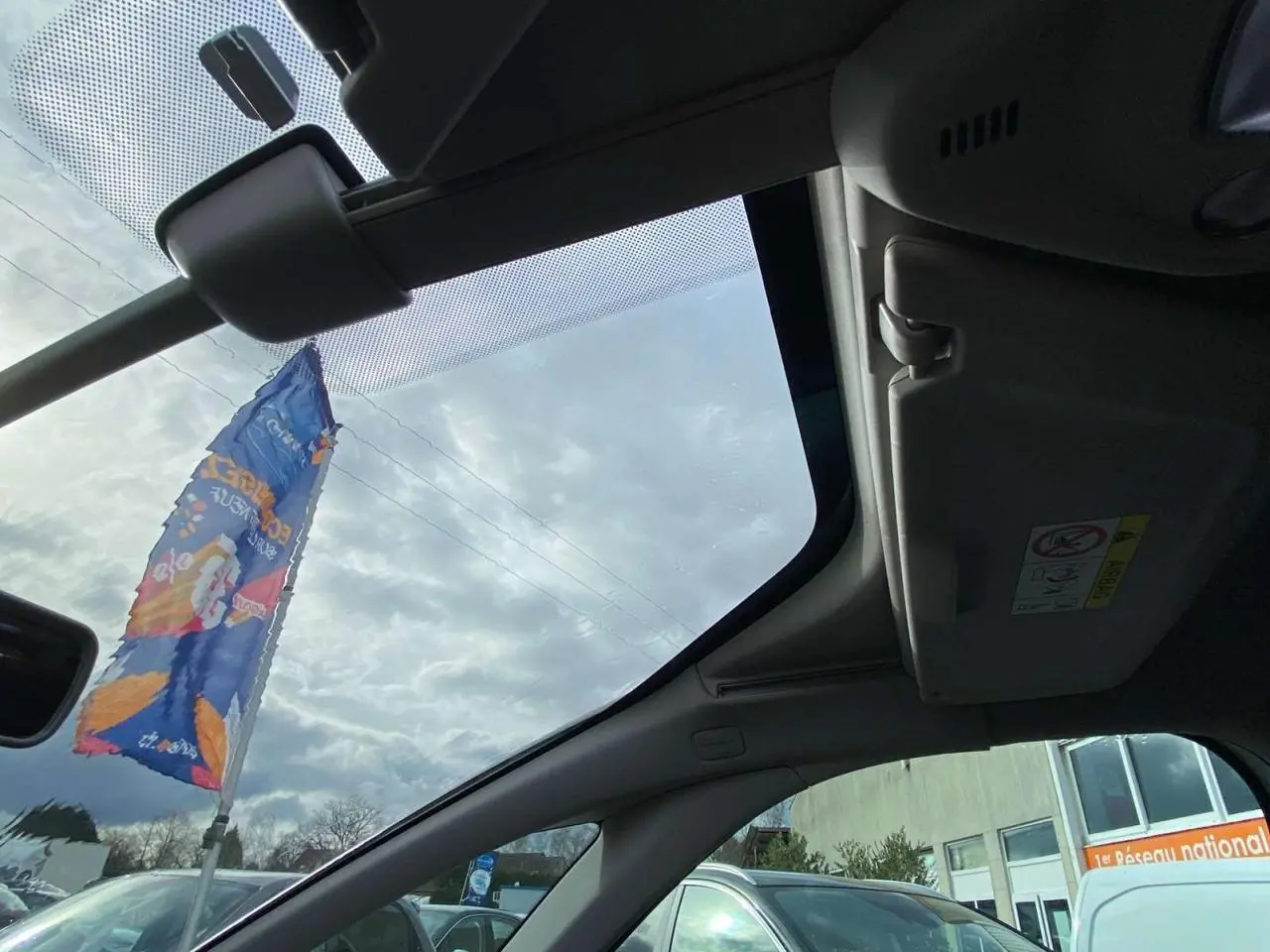 Vue intérieure du toit ouvrant panoramique du Citroën Grand C4 Picasso blanc, avec pare-soleil et ciel nuageux visible.