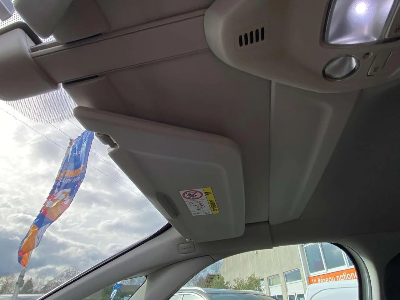 Vue intérieure côté conducteur du pare-soleil relevé et du plafond clair du Citroën Grand C4 Picasso blanc 2015.