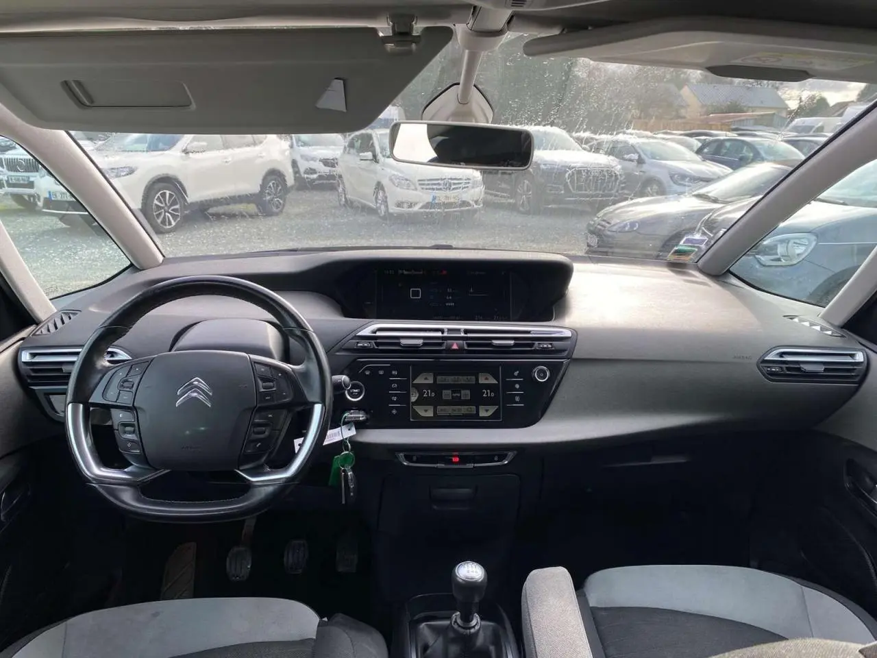 Intérieur du Citroën Grand C4 Picasso blanc 2015, vue frontale du tableau de bord avec volant cuir et boîte manuelle.