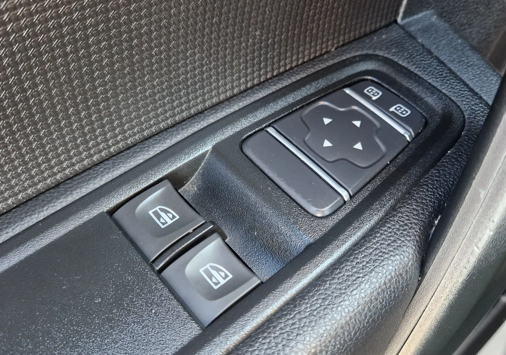 Gros plan sur les commandes des vitres et rétroviseurs électriques côté conducteur d’un Renault Kangoo blanc 2024.